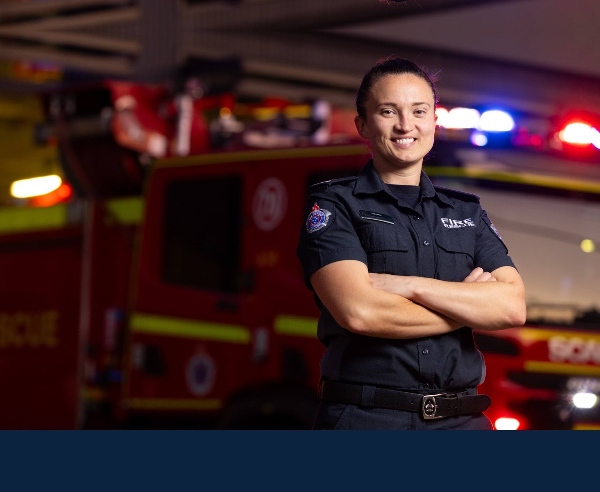 Woman firefighter standing in front of fire truck with arms crossed