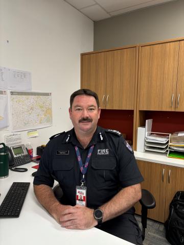 Photo of Commander Damien Scott, sitting behind a desk, smiling at camera.